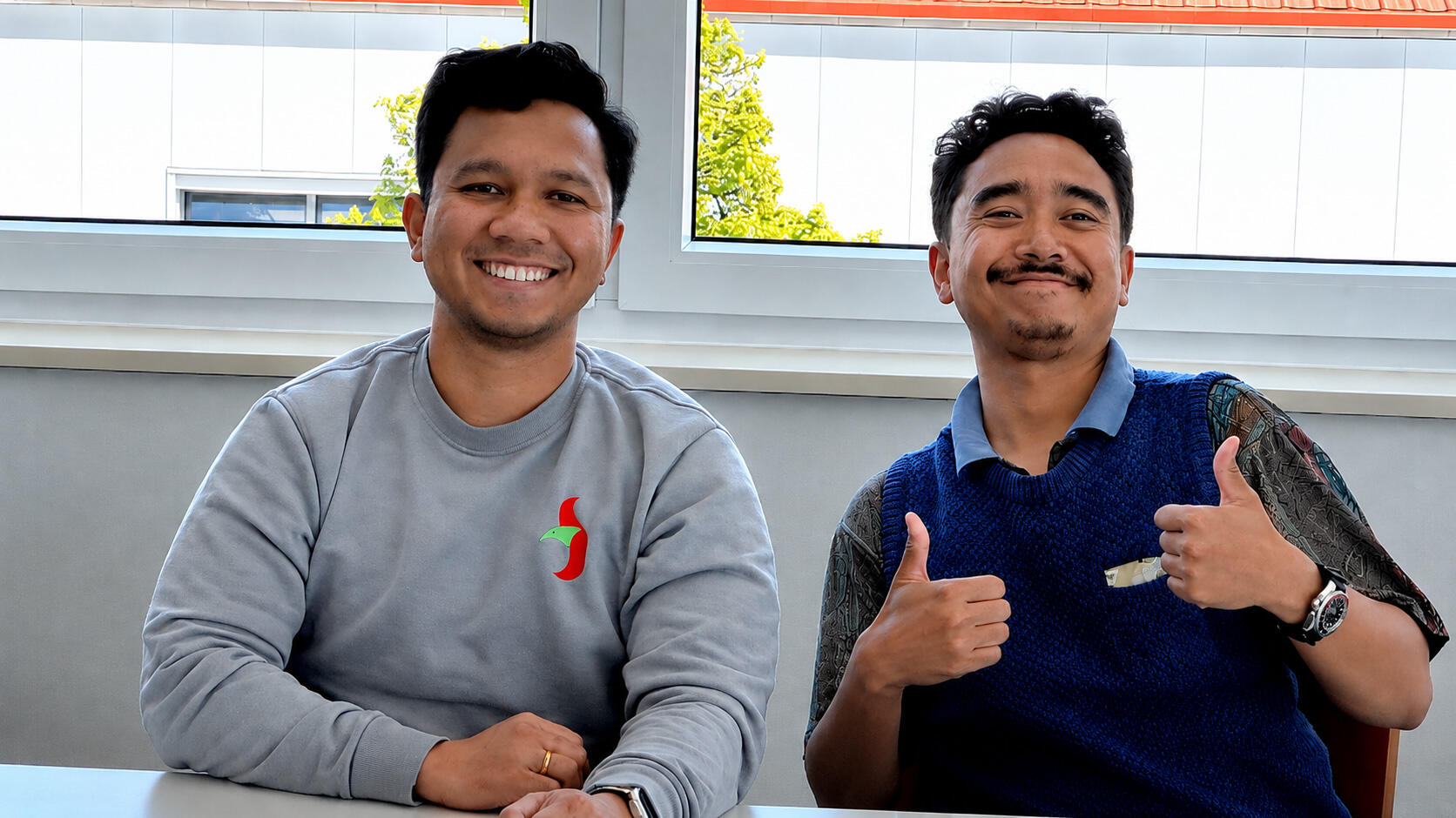 Two Indonesians are smiling at the camera; the man on the right is giving a thumbs-up