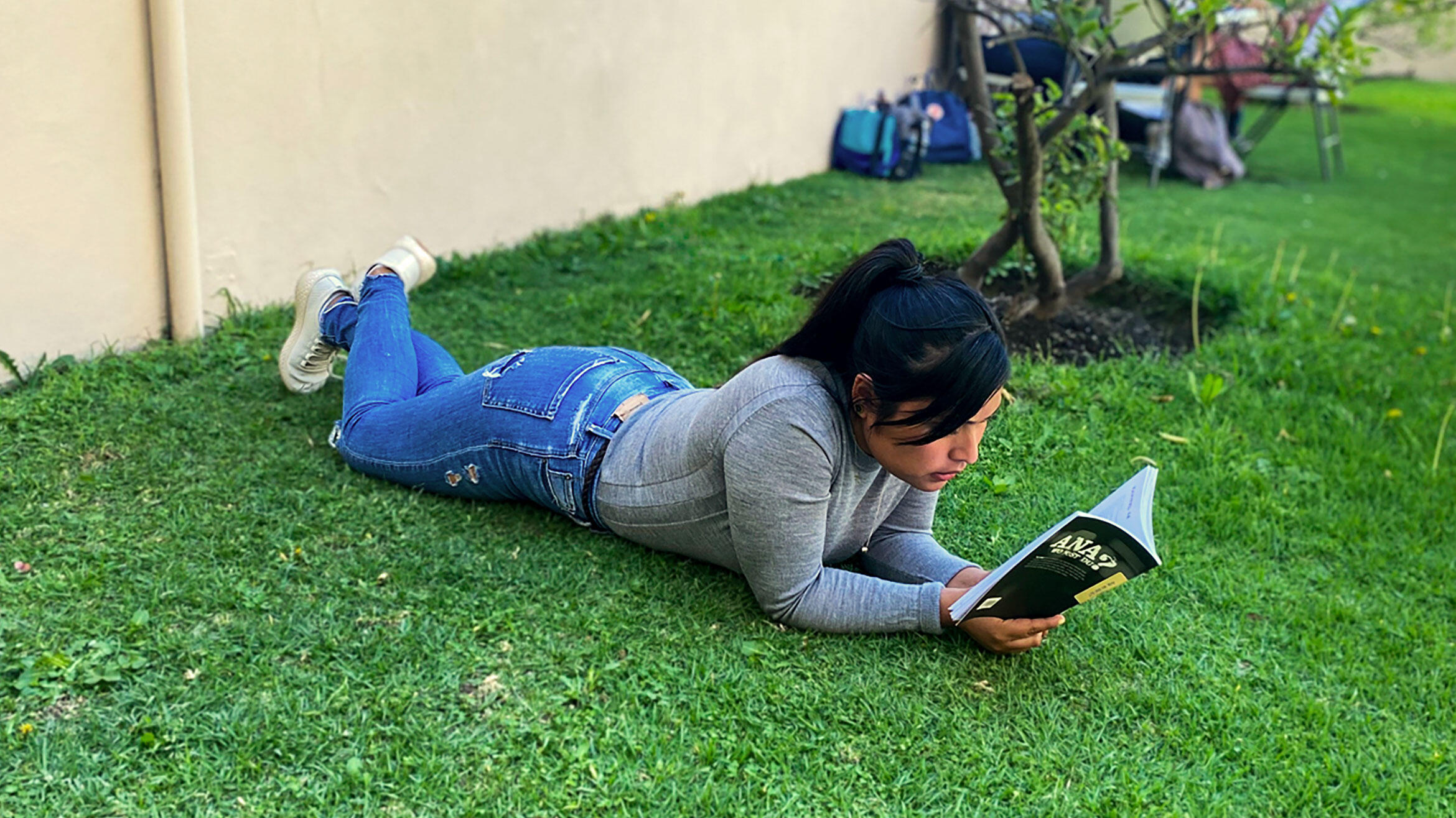 young Mexican woman lying on a meadow and reading a book
