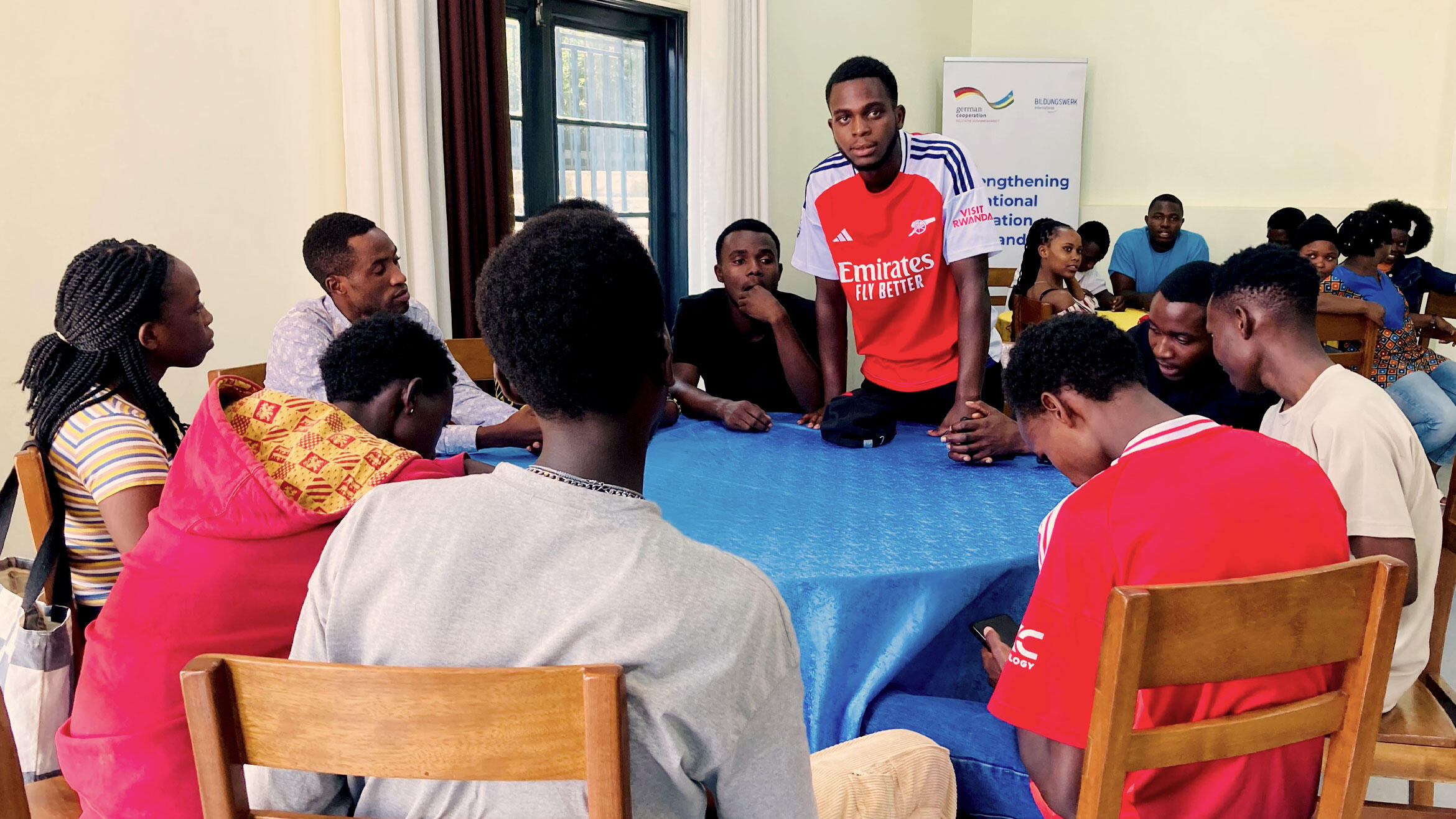 scene in a classroom, a person is speaking to trainees sitting at a round table
