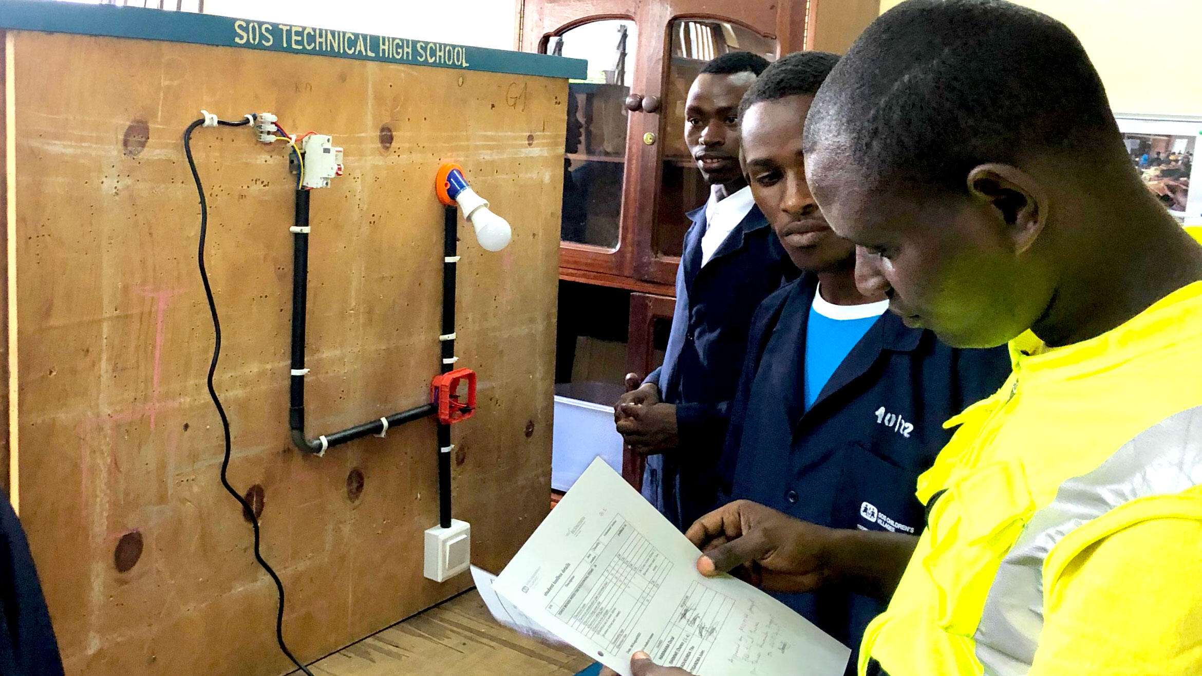 several Rwandans stand at a switchboard and study a document