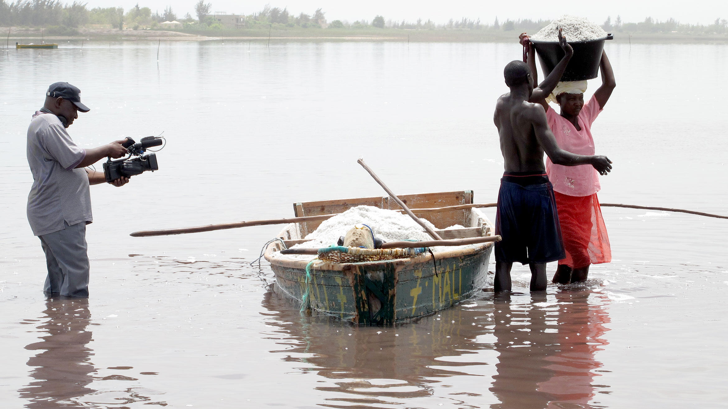 African cameraman films two people who are recovering salt at a lake