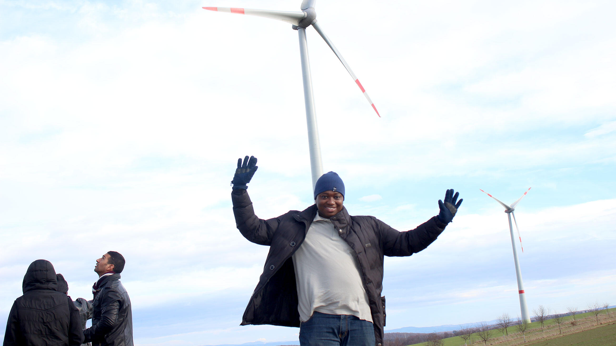 young African stands under windmills and waves into the camera