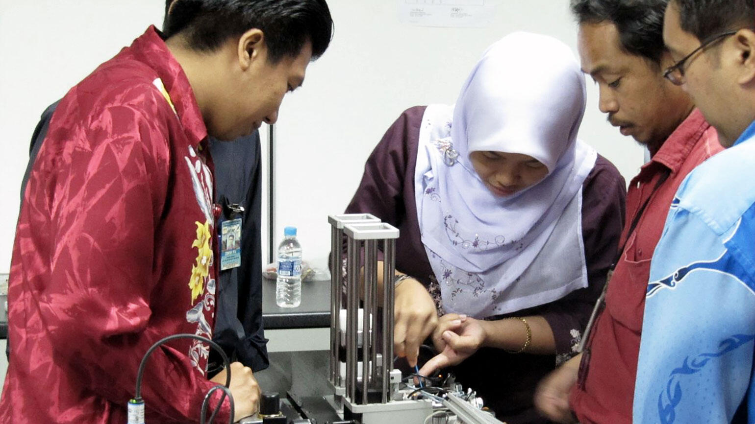 two men and a woman from Malaysia working in a workshop