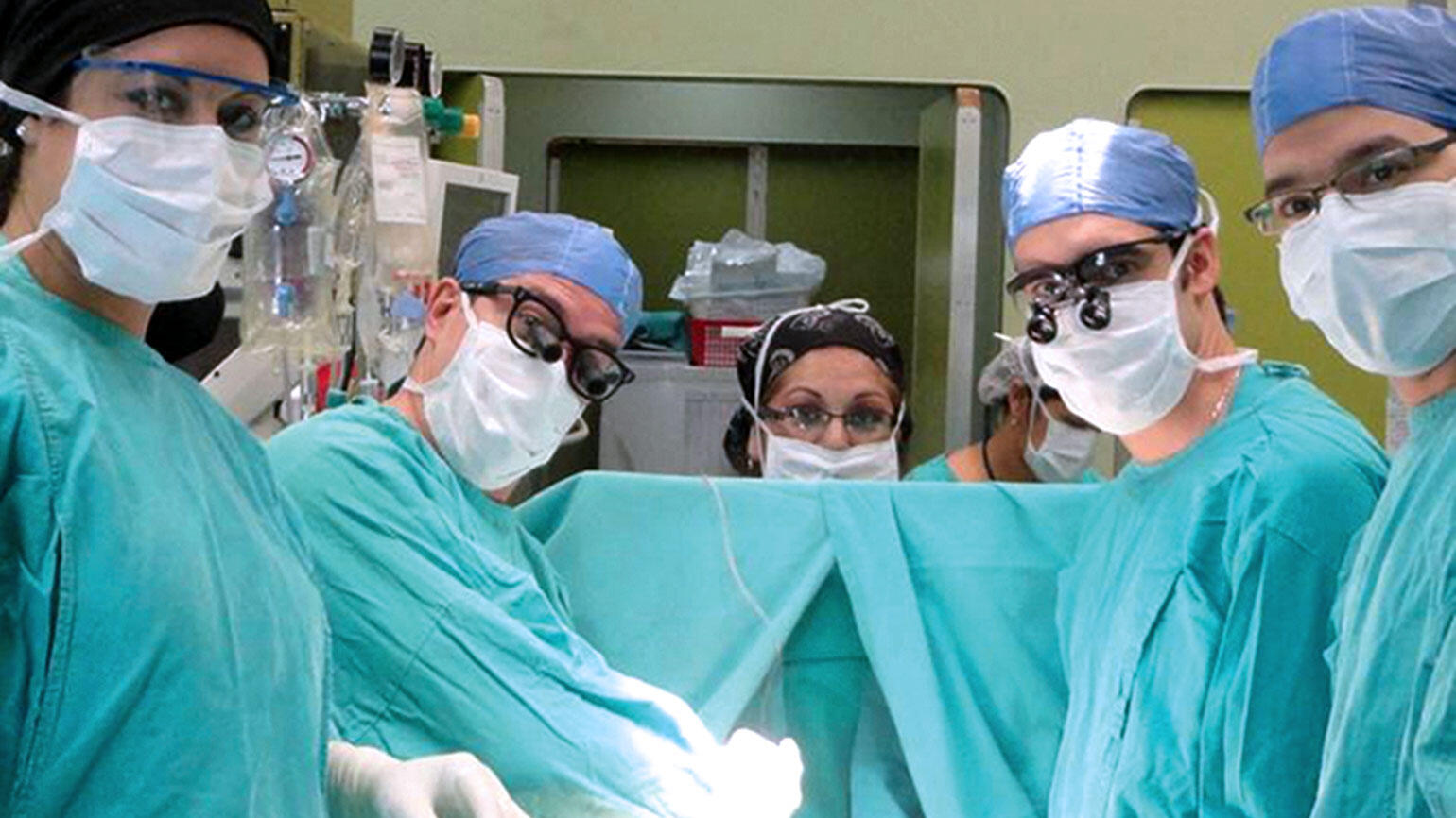several doctors in an operating theatre look into the camera