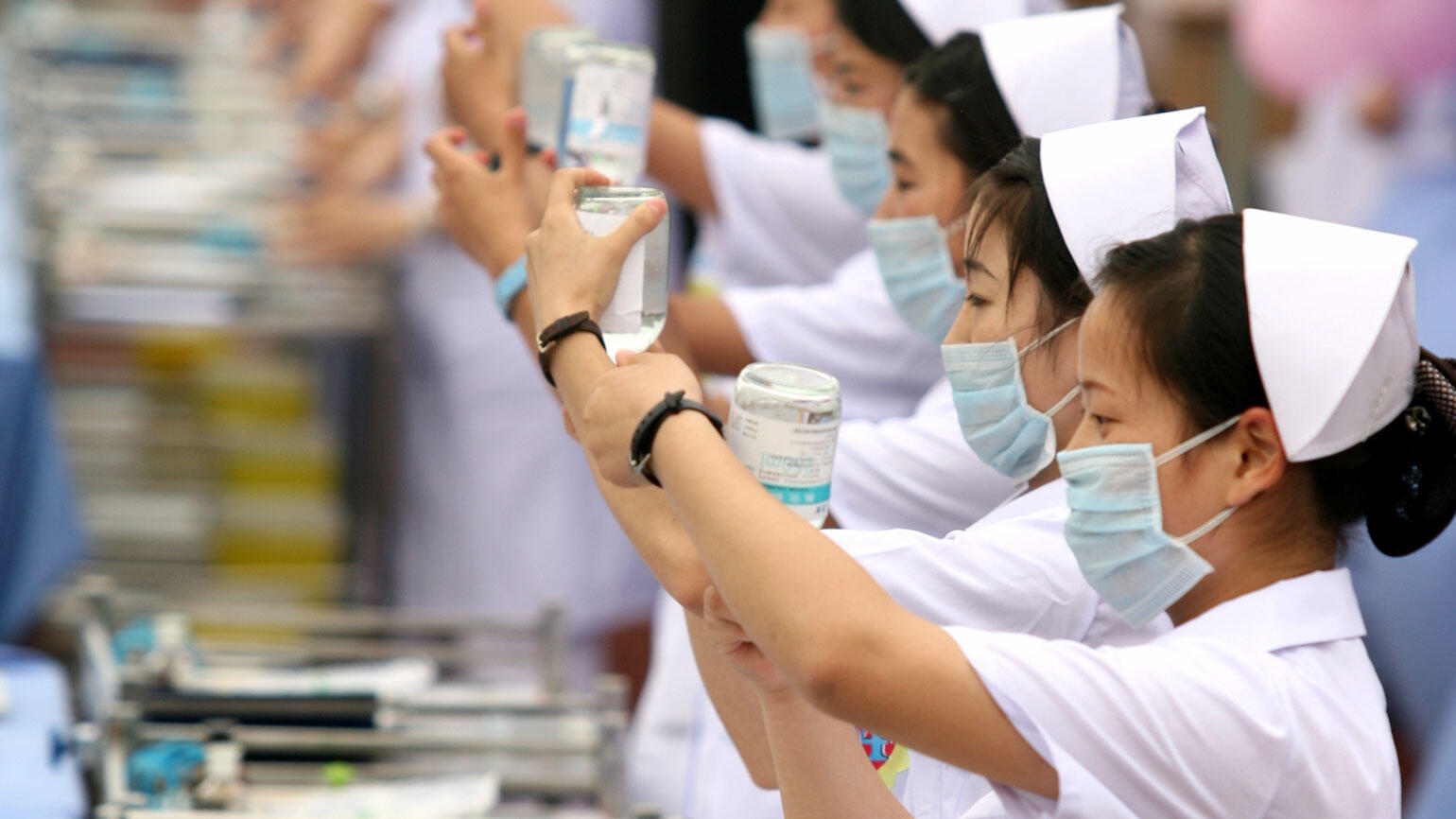 Chinese women in white coats stand in a row and draw syringes