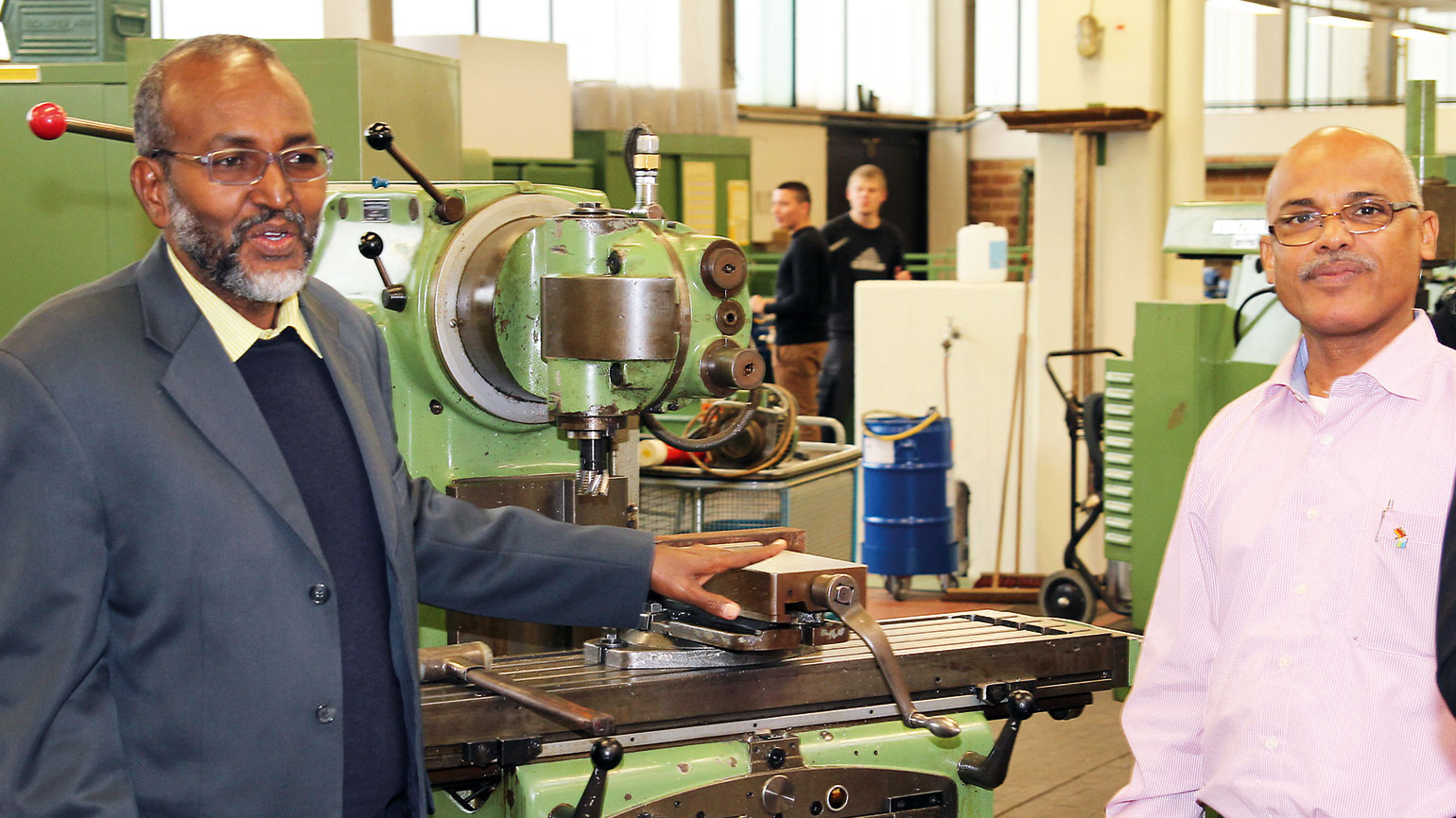 two men in a workshop stand at a machine