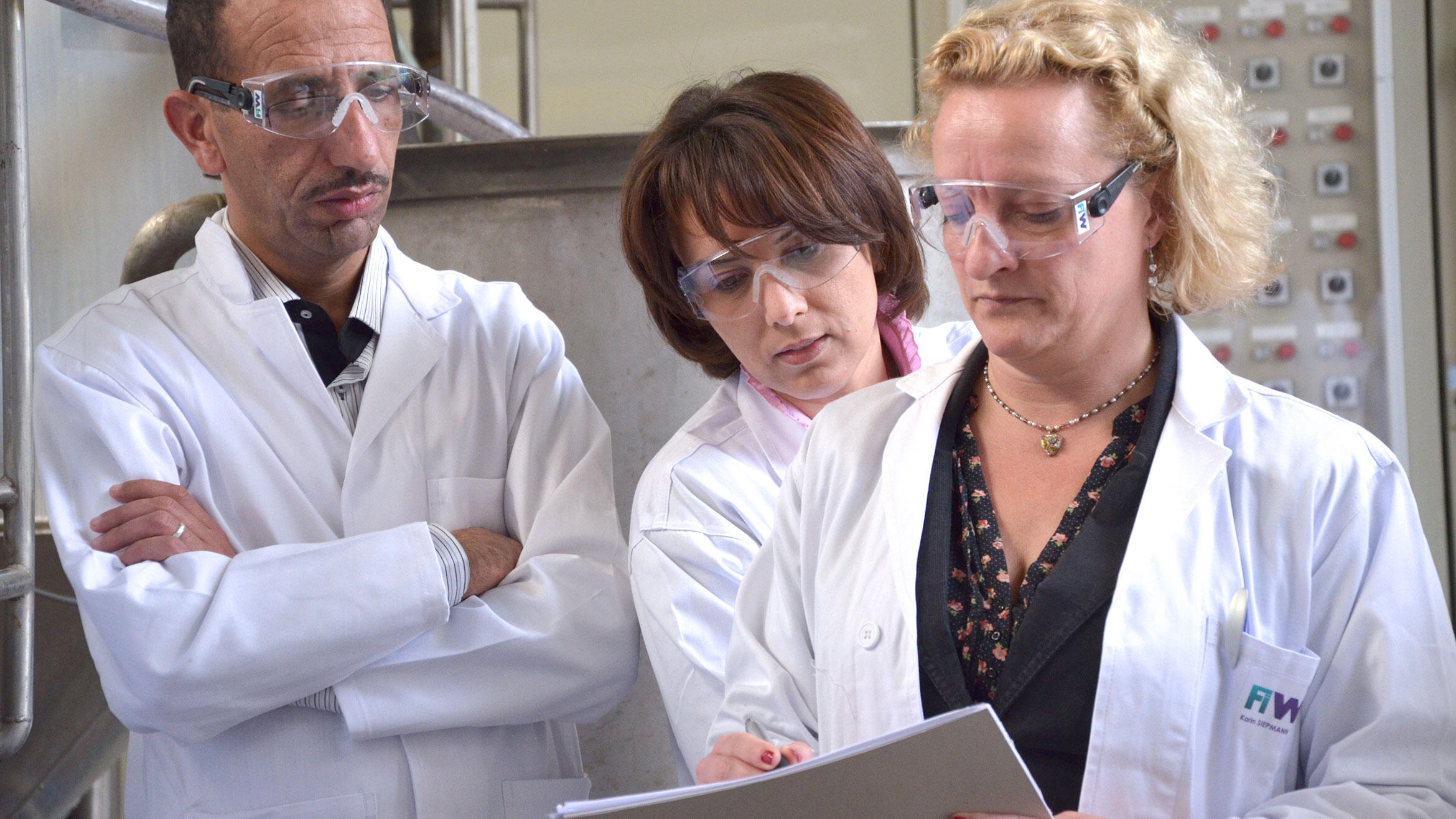 three people in white coats study together one document