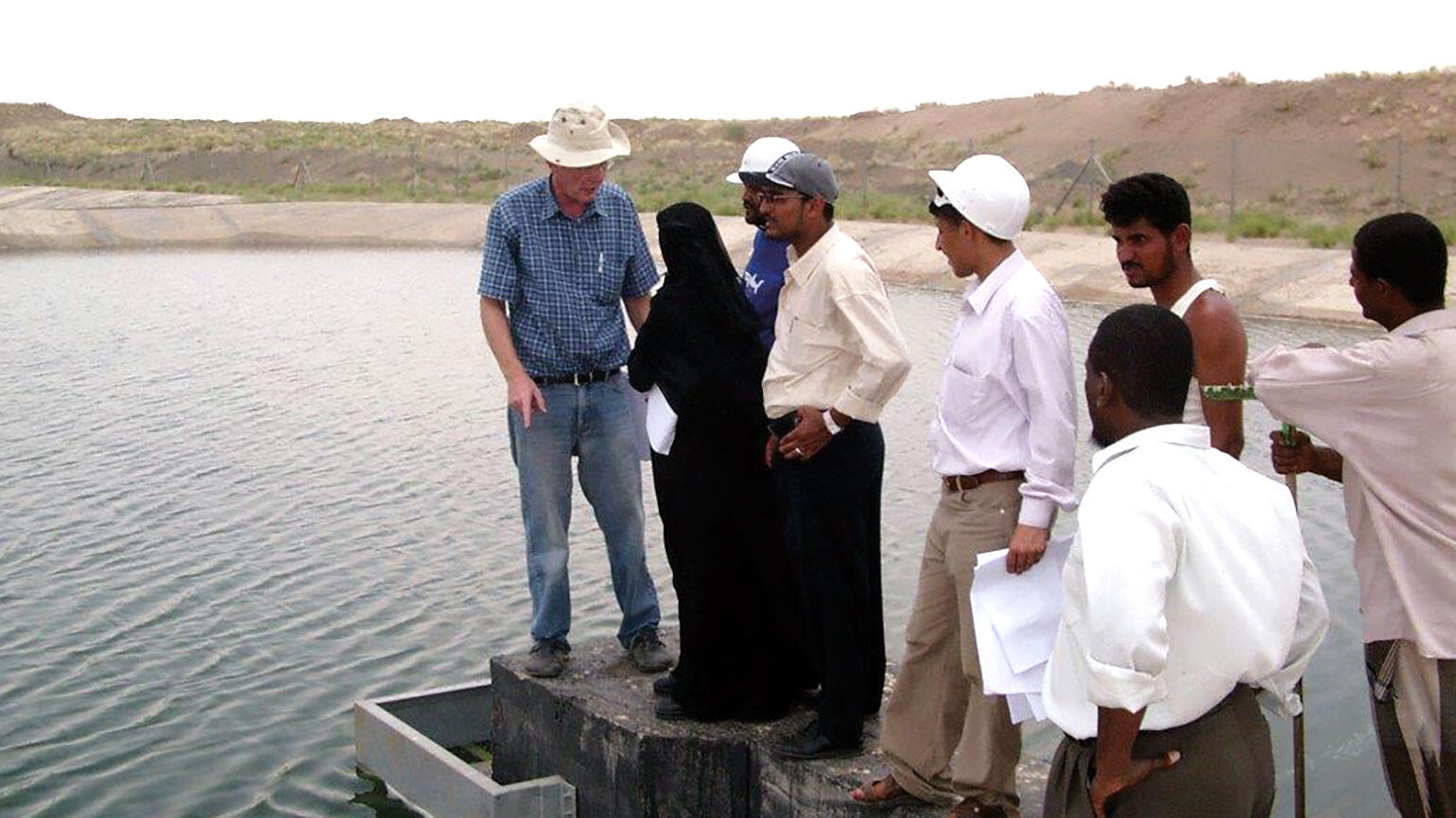 A group of people from the MENA region stands at some water installation listening to a trainer