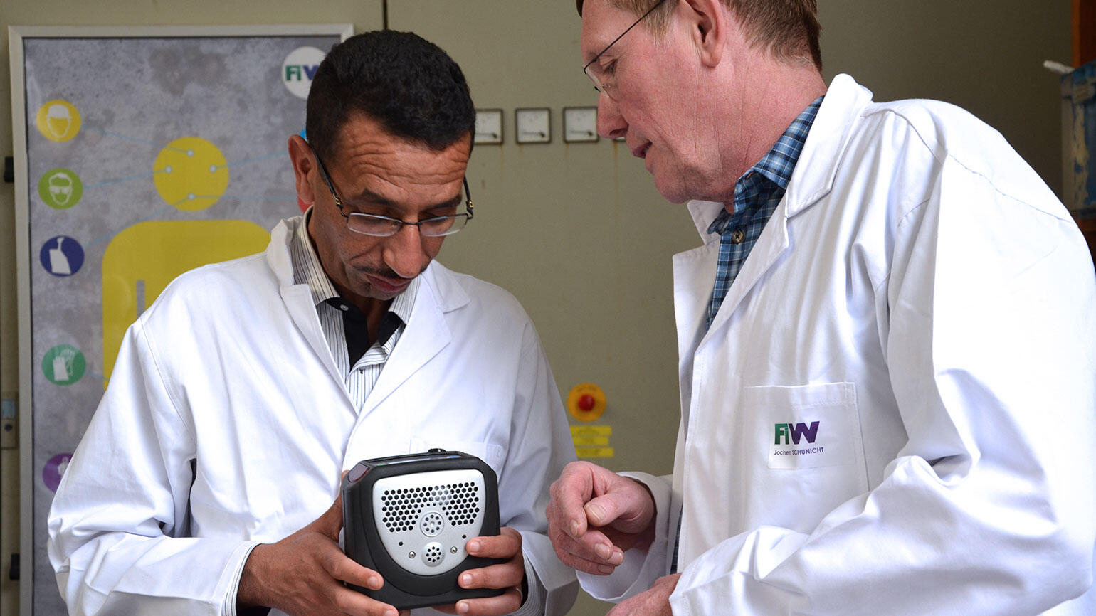 two men from Tunesia and Germany in white coats study some apparatus used in the water sector