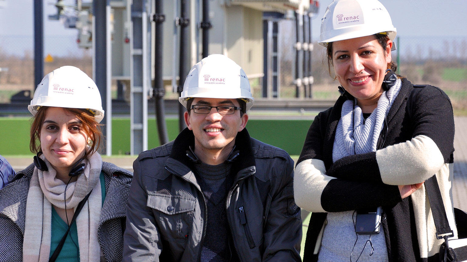 three people wearing safety helmets smile into the camera