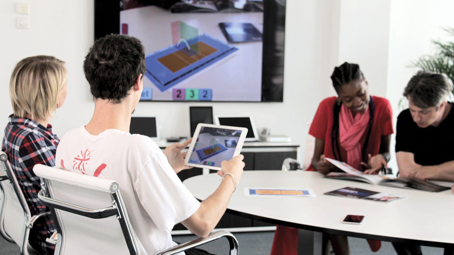 four men and women sit at a conference table and work with digital media