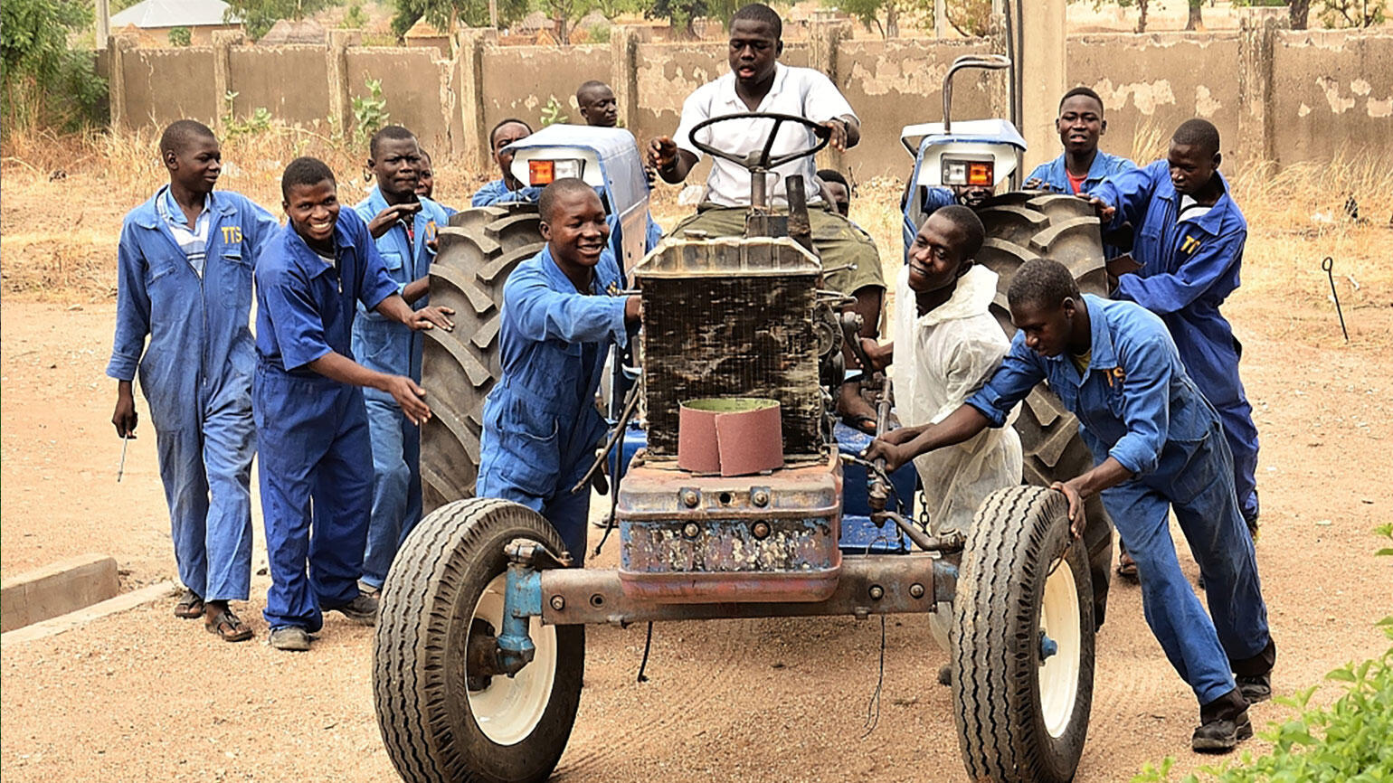 young men from nigeria push a tractor