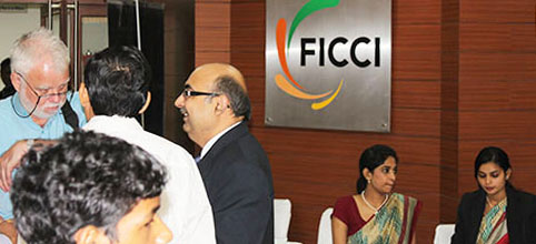 several people talking in front of the FICCI logo