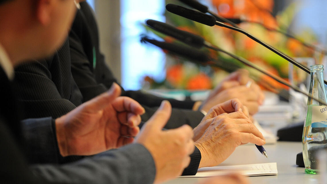 detailed view: hands and microphones on a speaker's desk