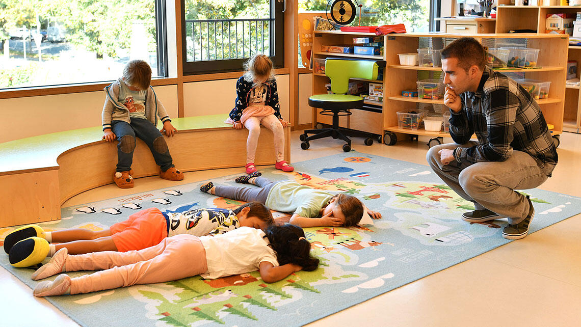 Scene from a childcare setting: children lie or sit down to rest under the supervision of an adult