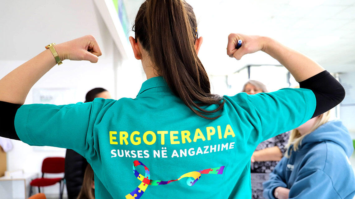 woman photographed from behind, her polo shirt reads occupational therapy in Kosovar