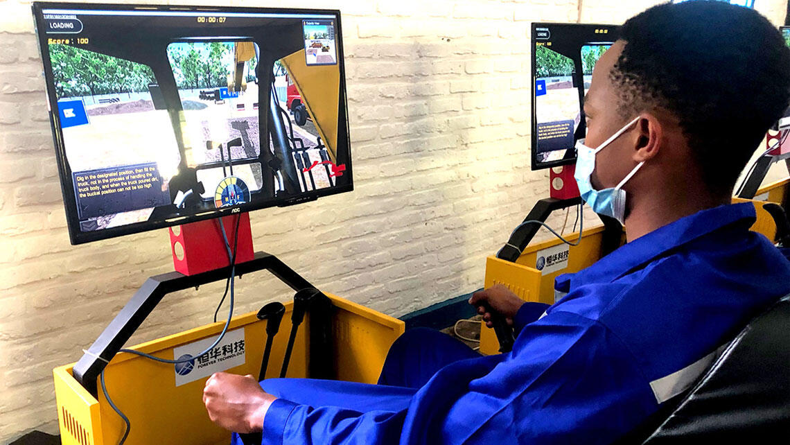 a man from Rwanda practices driving a construction machine on a simulator