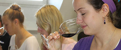 in the foreground a young woman with closed eyes holding a wine glass