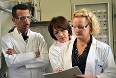 two women and a man in white work coats looking at a sheet of paper