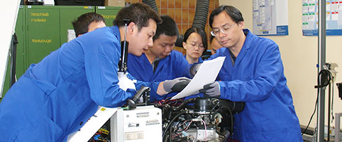 several Chinese trainees in blue overalls being trained on a machine