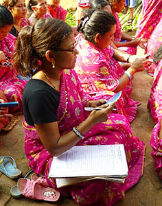 Women in Nepal in pink dresses sitting on the floor with notepads