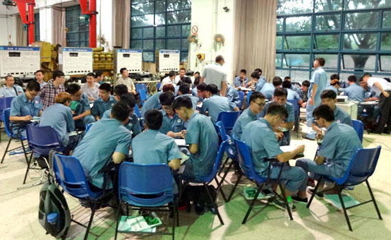 several chinese people sitting in small groups around tables and working together on something