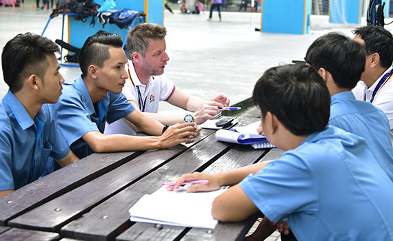 Men from Germany and Thailand sit around a table and talk to eachother