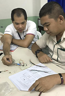 Two Thai men sitting at a table, one man shows the other one something in a document