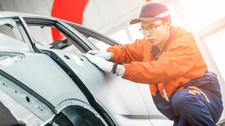 young Chinese man in work clothes crouches next to a car